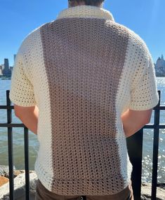 the back of a man wearing a crochet sweater standing next to a lake