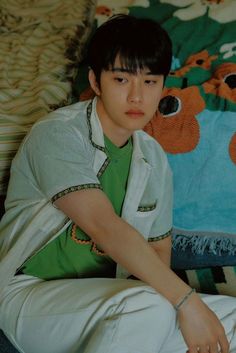 a young man sitting on top of a bed next to a teddy bear throw pillow