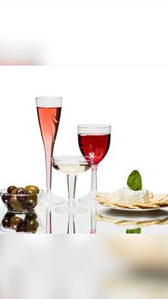 three glasses of wine and two plates with olives on the table next to each other