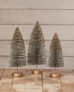 three small silver christmas trees sitting on top of a wooden table