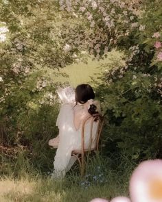 a woman sitting on top of a wooden chair under a tree