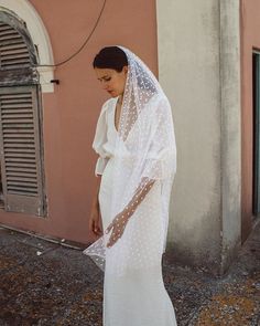 a woman in a white dress and veil is standing on the side of a building