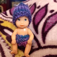 a small doll sitting on top of a purple and white blanket