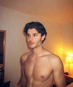 a shirtless man standing in a bedroom next to a lamp