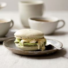 a sandwich on a plate with coffee cups in the background