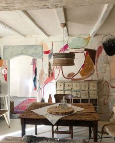 an old table and some chairs in a room with paintings on the wall behind it