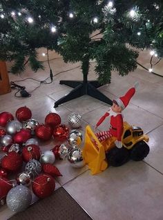 an elf on a toy tractor surrounded by christmas balls and ornaments in front of a tree