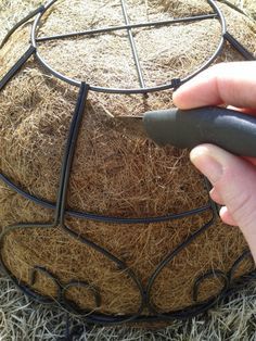 a hand is holding a black object in front of a round structure with grass growing on it