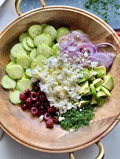 a wooden bowl filled with cucumbers, onions, cheese and other foodstuffs