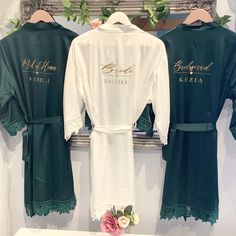 two robes are hanging on the wall in front of a mirror with flowers and greenery