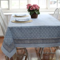 a blue table cloth with a basket of pink flowers on it and place settings at the top