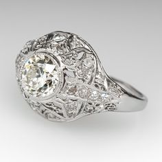 This gorgeous circa 1920s engagement ring features a domed pierced design and bordered with milgrain edging. The ring is centered with one (1), bezel set, old European cut diamond weighing 1.29 carats. The ring is accented with twenty-six (26), bead set, old European/single cut diamonds. The ring measures 13.8mm at the top, rises 7.3mm above the finger, tapering to 1.7mm wide and 0.7mm thick at the base of the shank. The ring is currently a size 7 and we offer complimentary resizing to fit. The ring is in good condition showing normal light wear. 1920s Engagement Ring, Antique Filigree, Bead Set, November Birthstone, European Cut Diamonds, High Quality Jewelry, Bezel Setting, Estate Jewelry, Diamond Cuts