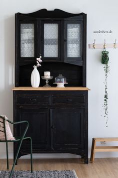 a black china cabinet with glass doors and flowers on top