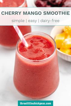 cherry mango smoothie in a glass with a pink straw on the top and another bowl of fruit behind it