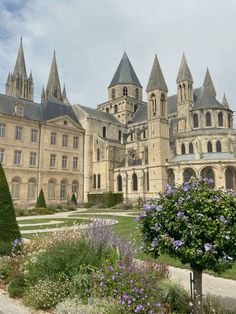 a large building with many towers on top of it's sides and purple flowers in the foreground