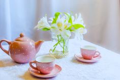 a table topped with pink cups and saucers next to a vase filled with flowers