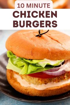 a chicken burger with lettuce, tomato and cheese on a black plate next to onion rings