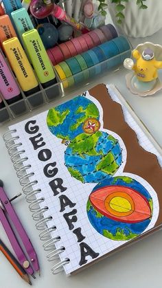 there is a notebook with the earth on it next to crayons and markers