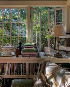 a room with many books and vases on top of the table in front of two windows