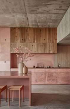 a pink kitchen with wooden cabinets and stools