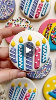 a person holding a decorated cookie in front of many other decorated cookies on a table