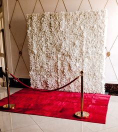 a red carpet on the ground in front of a wall with white flowers and gold poles