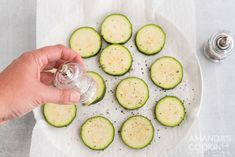 a person is holding a glass bottle over some cut up cucumbers on a plate