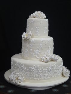 a three tiered wedding cake with white frosting flowers and lace on the top