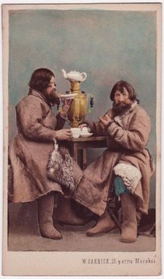 two people sitting at a table with a vase in the background and one holding a cup