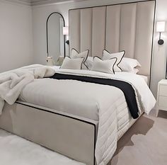 a bed with white sheets and pillows in a bedroom next to a large mirror on the wall