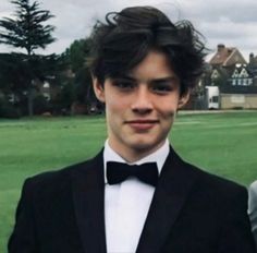 two young men in tuxedos are posing for a photo outside on the grass