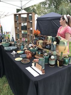 a woman standing in front of a table covered with plates and vases at an outdoor market