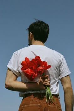 a man holding red flowers in his hands and looking up at the blue sky behind him