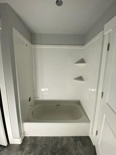 an empty bathtub in a white bathroom with gray tile flooring and grey walls