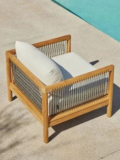 a wooden lounge chair sitting next to a swimming pool with pillows on it's back