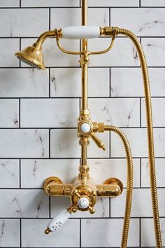 a gold faucet and shower head in a white tiled bathroom with brass fixtures