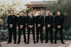 a group of men standing next to each other in front of a tree and bushes