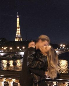 a man and woman kissing in front of the eiffel tower, at night