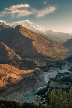 the mountains are covered with snow and green trees in the foreground is a river running through it