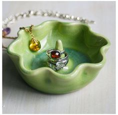 a green bowl with a ring on it and a chain hanging from the side, sitting on a table