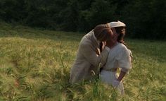 two people are kissing in the middle of a field with tall grass and trees behind them