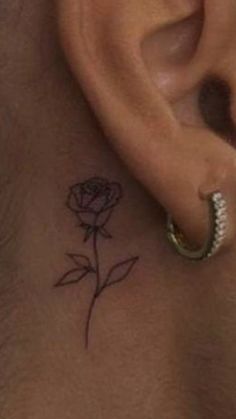 a close up of a person's ear with a small rose tattoo on it