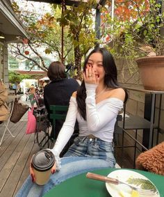 a woman sitting at an outdoor table holding her hands up to her face and covering her mouth