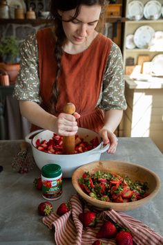 a woman is mixing strawberries in a bowl with a wooden spoon on the table