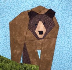 a bear made out of brown paper sitting on top of green grass next to a blue background