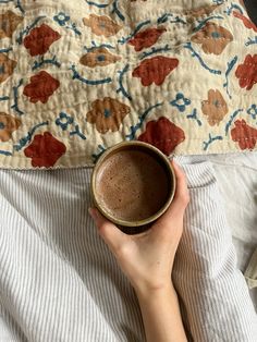 a person is holding a coffee cup while laying in bed