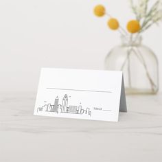 a card with a city skyline drawn on it next to a vase filled with flowers