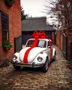 an old white car with a red ribbon tied around it's hood parked in front of a brick building