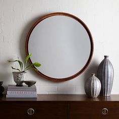 a round mirror sitting on top of a wooden dresser next to vases and books