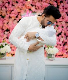 a man holding a baby in front of a flower wall with pink and white flowers